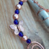 A strand of round beads, blue glass alternating with copper, with a coppery butterfly caught in between.
