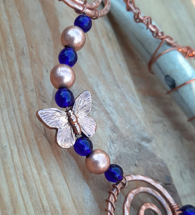 A strand of round beads, blue glass alternating with copper, with a coppery butterfly caught in between.