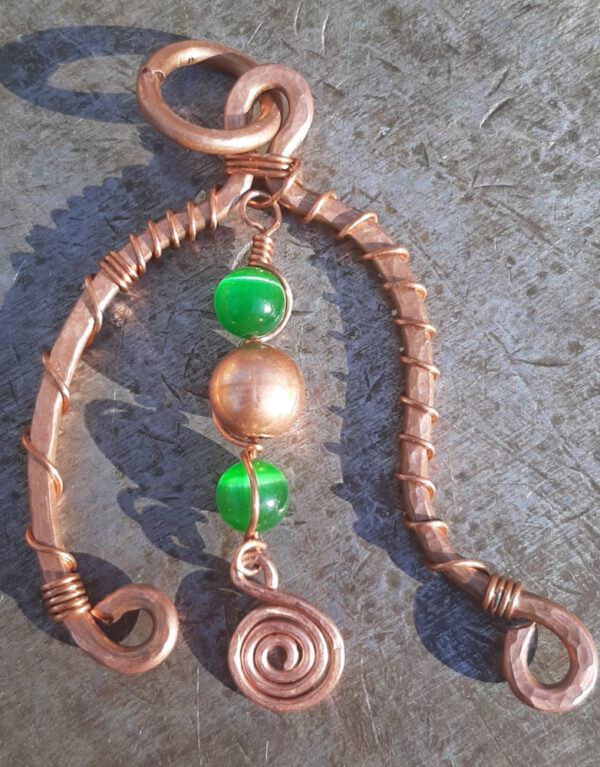 An asymmetrical arch in copper wire -- one end turned inwards, the other curved out. Hanging down the middle are two green glass beads with a copper one between them, all threaded onto thin copper wire.