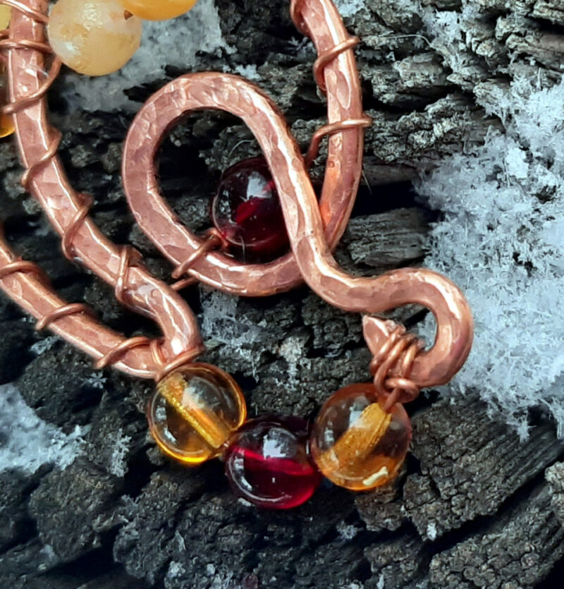 A curving, looping shape in copper wire is adorned with round glass beads ranging in color from yellow through various ambers to red.