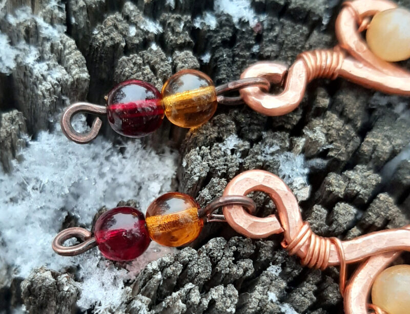 Each earring curves hammered copper down into and through a single loop with a pale yellow glass bead; two more, amber then deep red, hang below.