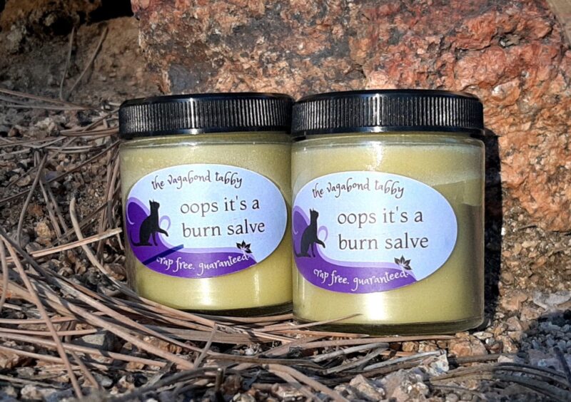 Two big clear glass jars filled with pale yellow salve. The labels say 'oops it's a burn salve'.