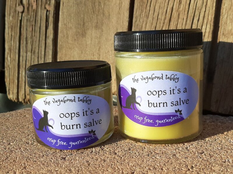 Two clear glass jars, one bigger than the other, filled with pale yellow salve. The labels say 'oops it's a burn salve'.