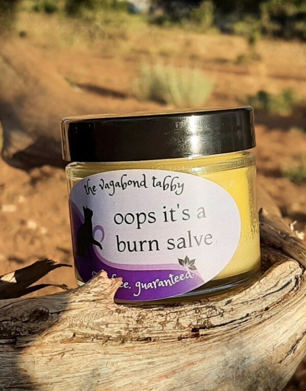 A small clear glass jar filled with pale yellow salve. The label says 'oops it's a burn salve'.