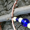 The spot where the copper arc meets the driftwood. Thinner copper wire wraps around the thick stuff, ducking under the stick to hold the two together before heading off, bearing blue and white beads.