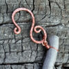 The hook at the top of the piece, a simple s-shape with loops on either end, in hammered copper wire.