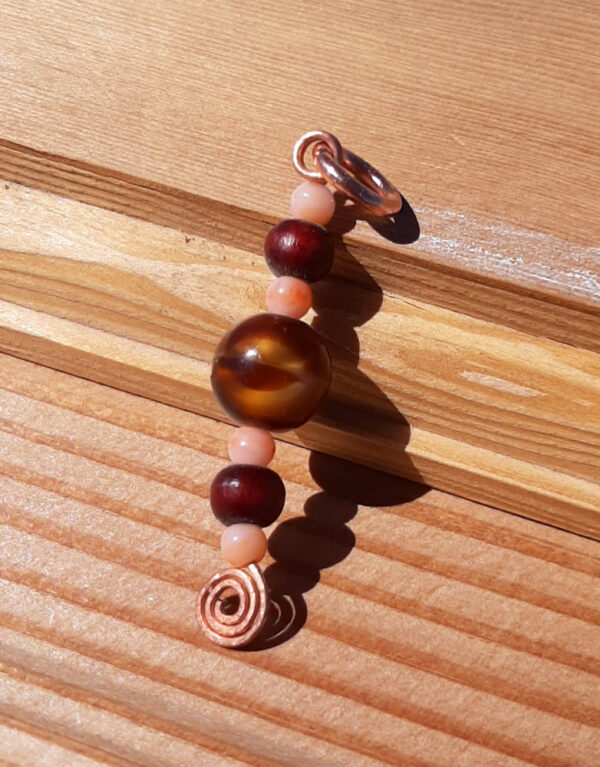 A single line of beads -- peach, reddish wood, and swirly gold and brown -- on a straight length of copper wire, with a hammered spiral at the bottom.