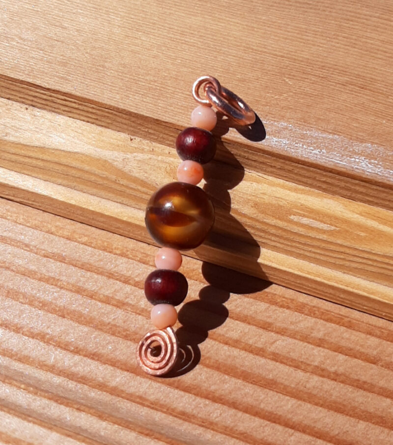 A single line of beads -- peach, reddish wood, and swirly gold and brown -- on a straight length of copper wire, with a hammered spiral at the bottom.
