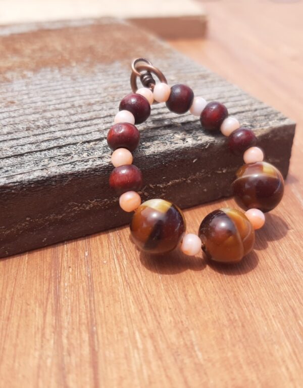 Beads, peach and reddish wood and stripey gold and brown, are threaded onto a simple loop of copper wire.