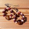 Each earring is a loop strung with alternating tiny peach beads and slightly bigger red wooden ones, with a larger stripey brown and gold bead at the bottom.
