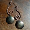 Each earring is hammered copper wire shaped like an inverted question mark. From the bottom hangs a domed brass circle, weathered til it looks a bit like a moon.