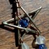 An interlaced star with a blue glass bead in the center. Two dangles of beads hang from the bottom two points, each holding a white, a blue, and a purple bead.