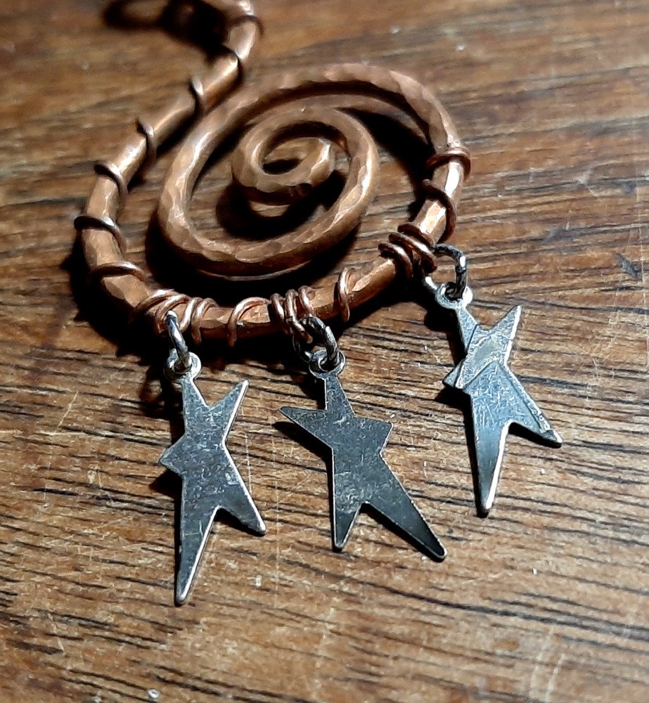 A wide spiral in hammered copper wire, with three tiny, flat, asymmetrical stars hanging from the bottom.