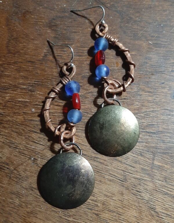 Hammered copper in a shallow c-shape, mirrored with strung beads, blue and red. Below hang domed brass circles, weathered til they resemble a moon.