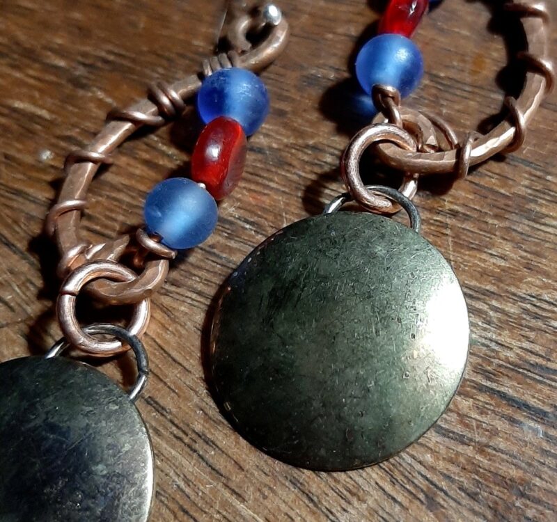Hammered copper in a shallow c-shape, mirrored with strung beads, blue and red. Below hang domed brass circles, weathered til they resemble a moon.