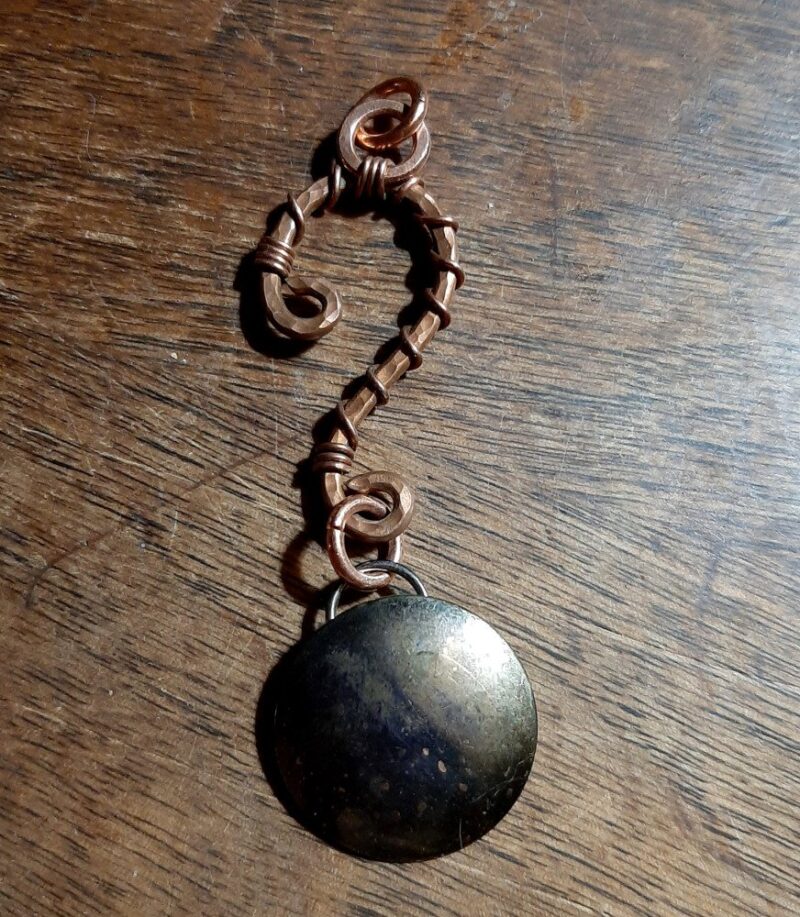 Hammered copper wire in the shape of a question mark. From the bottom hangs a domed brass circle.