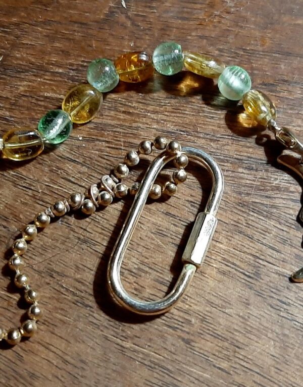 A pendulum. At the bottom hangs a narrow crescent moon, with a face in it. Next up are3 glass beads alternating pale green and amber, followed by a couple inches of gold-colored ball chain. At the top is a screw lock carabiner.