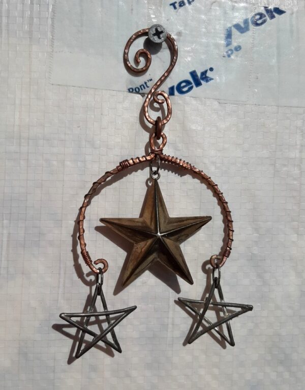 This pixy home decor piece features a semicircle of copper wire surrounding a star pendant. Smaller stars hang from each end of the semicircle.