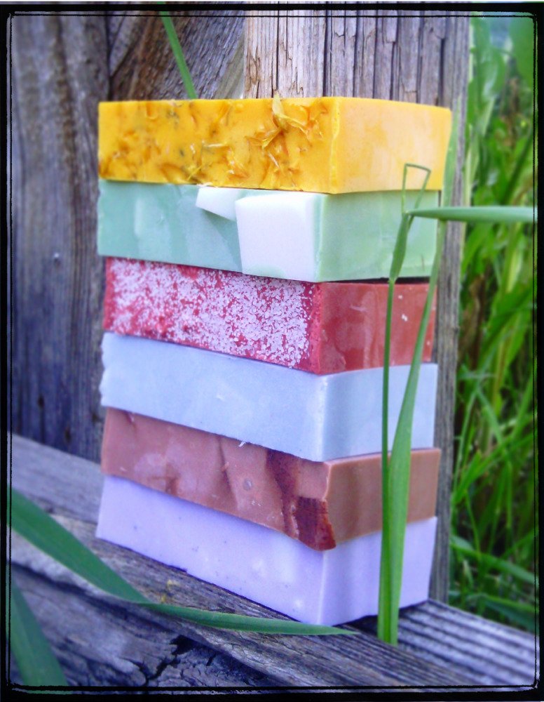 A stack of six bars of soap in various colors -- yellow, green, red, pale blue, variegated brown, and purple.