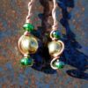 Each earring has round brass beads with oval green glass to either side, strung on copper wire that curves back up around each bead, then twists around itself.