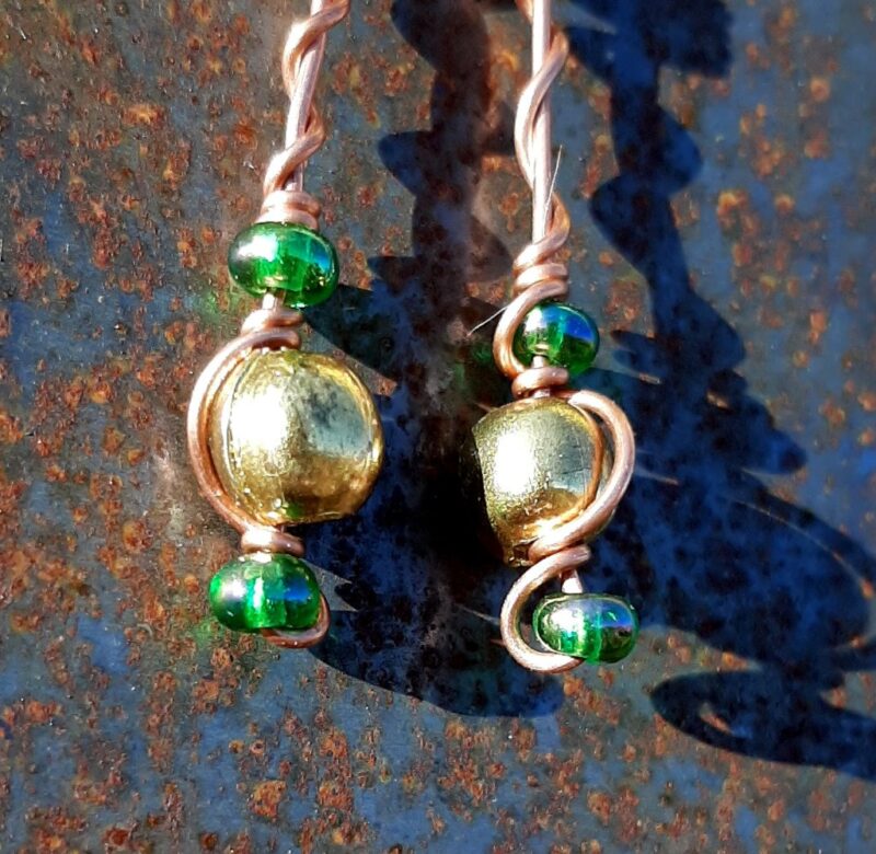 Each earring has round brass beads with oval green glass to either side, strung on copper wire that curves back up around each bead, then twists around itself.