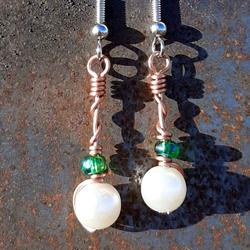 Each earring has a round white bead with an oval green glass bead above, strung on copper wire that curves back up around each bead, then twists around itself.