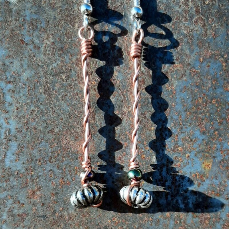 Each earring has an oval silver-colored bead with an iridescent green glass bead above, all strung on copper wire that curves back up around each bead, then twists around itself.
