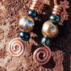 Each earring has a round brass bead with a deep green bead to either side, all strung on copper wire that ends at the bottom in a neat spiral.