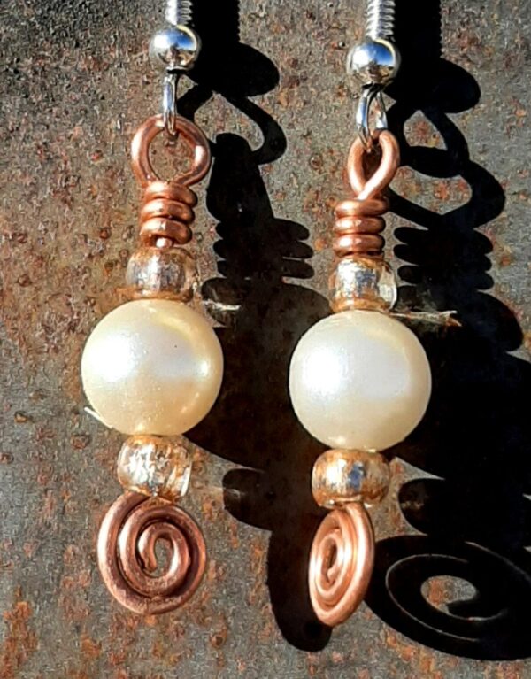 Each earring has a round white bead with a sparkly orange-brown bead to either side, all strung on copper wire that ends at the bottom in a neat spiral.