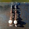 Each earring has round white beads with oval clear glass to either side, strung on copper wire that curves back up around each bead, then twists around itself.