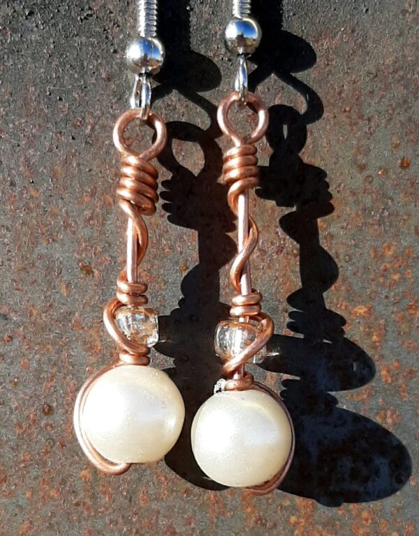 Each earring has a round white bead with a clear glass bead above, all strung on copper wire that curves back up around each bead, then twists around itself.