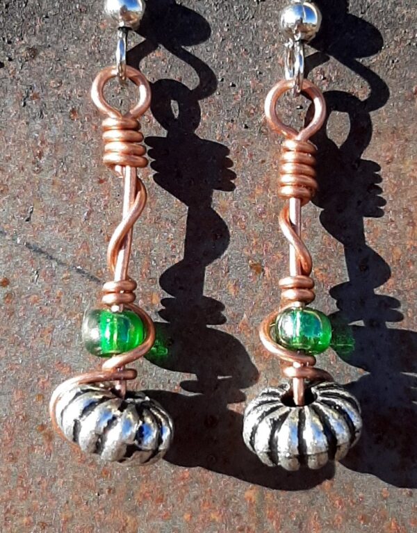 Each earring has an oval silver-colored bead with a green glass bead above, all strung on copper wire that curves back up around each bead, then twists around itself.