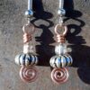 Each earring has an oval silver-colored bead with a clear glass bead above, all strung on copper wire that ends at the bottom in a neat spiral.