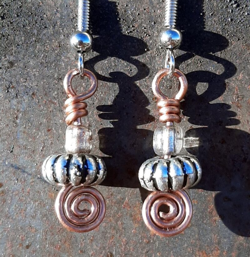 Each earring has an oval silver-colored bead with a clear glass bead above, all strung on copper wire that ends at the bottom in a neat spiral.