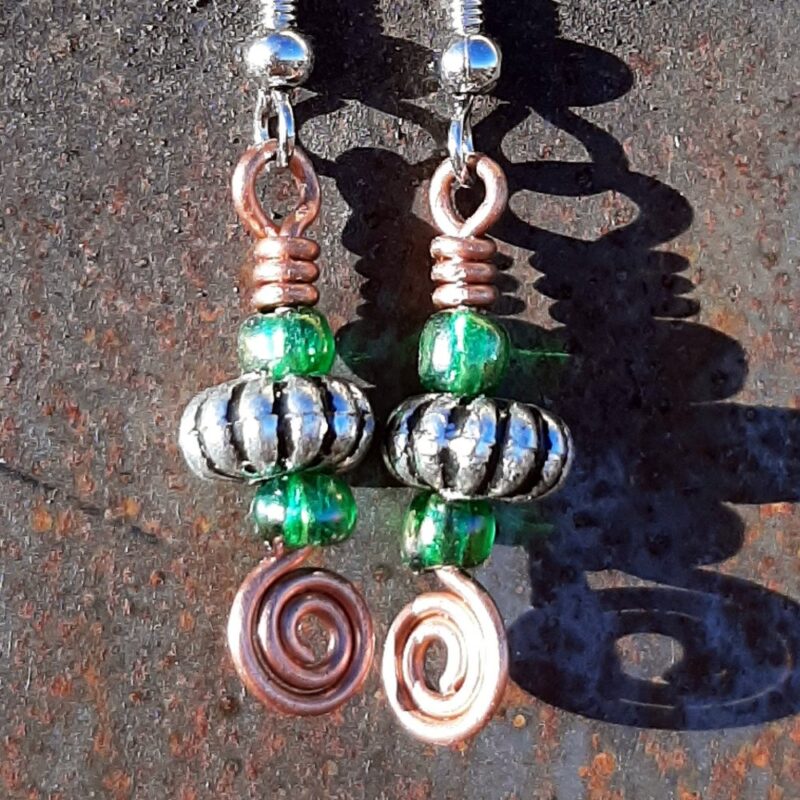Each earring has an oval silver-colored bead with a green glass bead to either side, all strung on copper wire that ends at the bottom in a neat spiral.