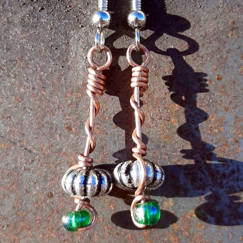 Each earring has an oval silver-colored bead with a green glass bead below, all strung on copper wire that curves back up around each bead, then twists around itself.