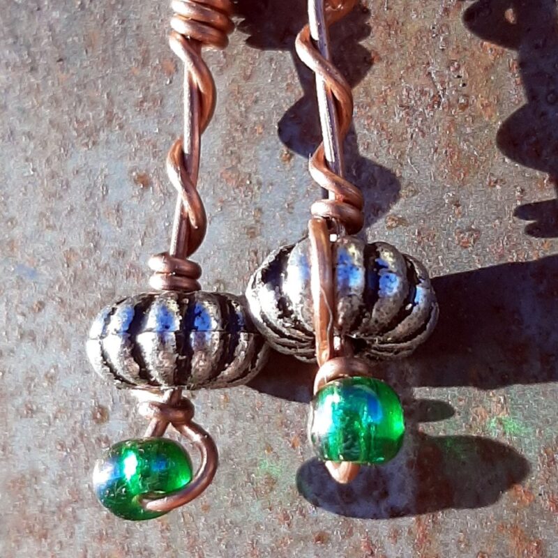 Each earring has an oval silver-colored bead with a green glass bead below, all strung on copper wire that curves back up around each bead, then twists around itself.