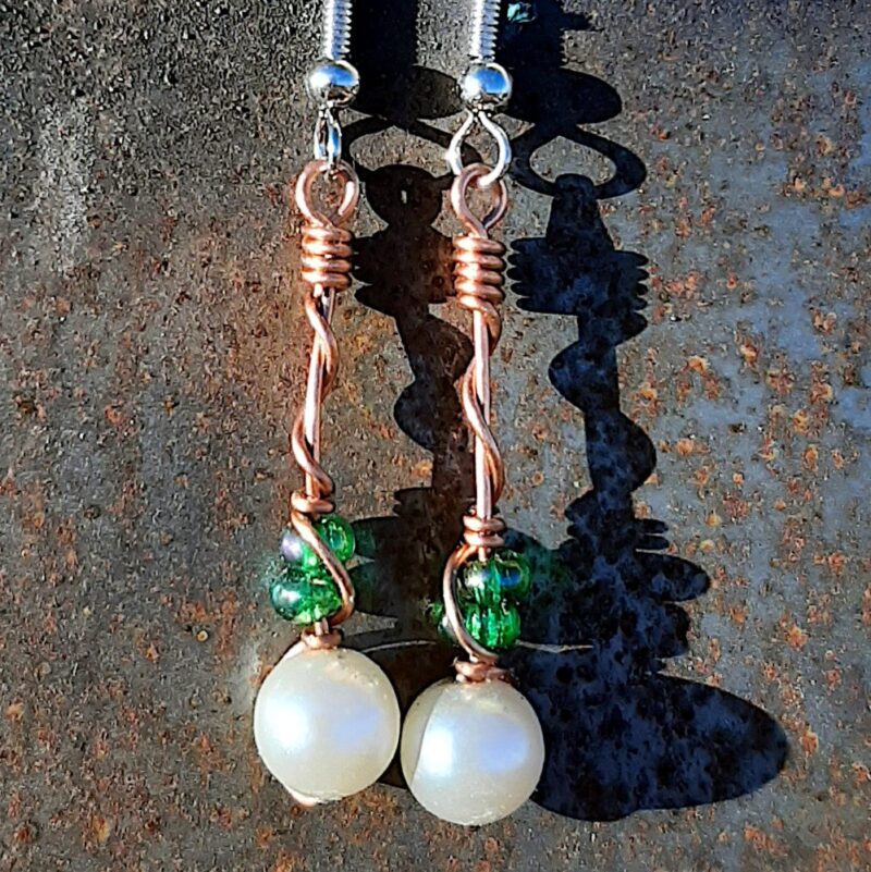 Each earring has round white beads with two oval green glass above, strung on copper wire that curves back up around each bead, then twists around itself.