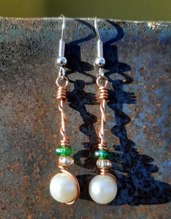 Each earring has a round white bead with a clear yellow glass bead and a green glass bead above, all strung on copper wire that curves back up around each bead, then twists around itself.