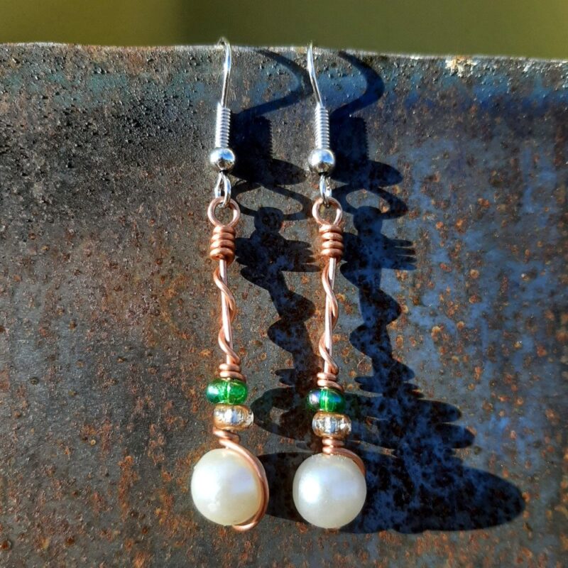 Each earring has a round white bead with a clear yellow glass bead and a green glass bead above, all strung on copper wire that curves back up around each bead, then twists around itself.