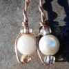 Each earring has round white beads with oval clear glass to either side, strung on copper wire that curves back up around all three beads, then twists around itself.