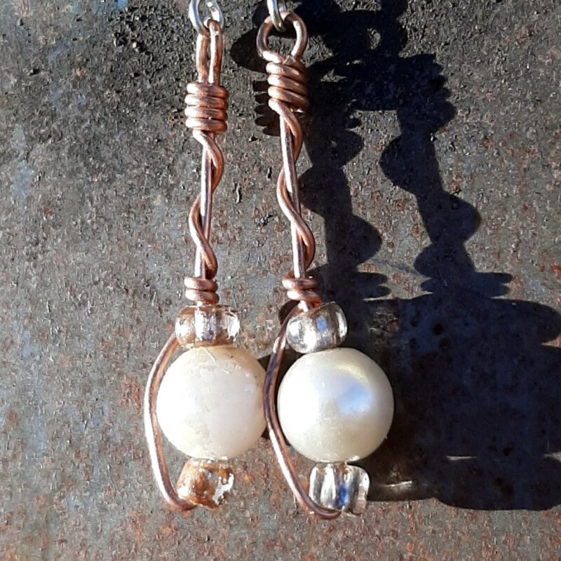 Each earring has round white beads with oval clear glass to either side, strung on copper wire that curves back up around all three beads, then twists around itself.