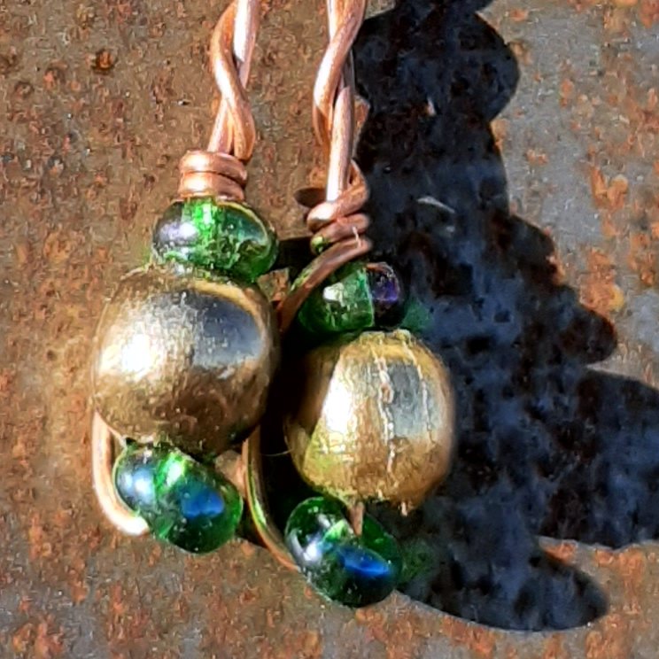 Each earring has round brass beads with oval green glass to either side, strung on copper wire that curves back up around the three beads, then twists around itself.