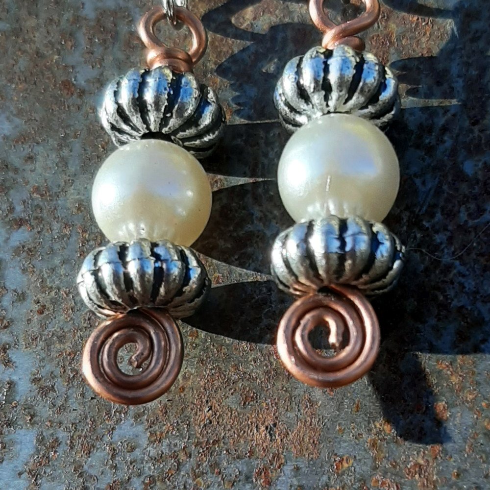 Each earring has a round white bead between two oval silver-colored beads, all strung on copper wire that ends at the bottom in a neat spiral.