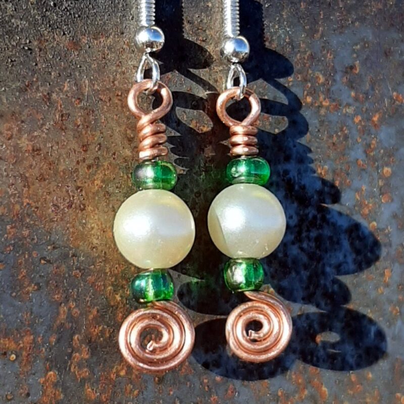 Each earring has a round white bead with a kelly green bead to either side, all strung on copper wire that ends at the bottom in a neat spiral.