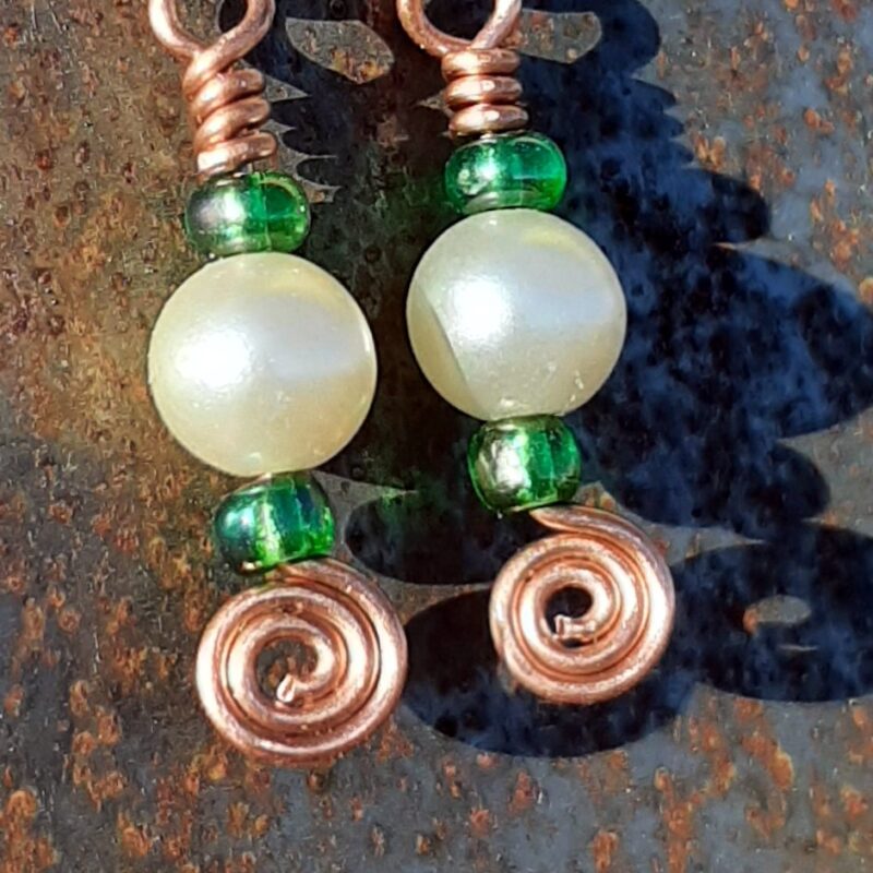 Each earring has a round white bead with a kelly green bead to either side, all strung on copper wire that ends at the bottom in a neat spiral.