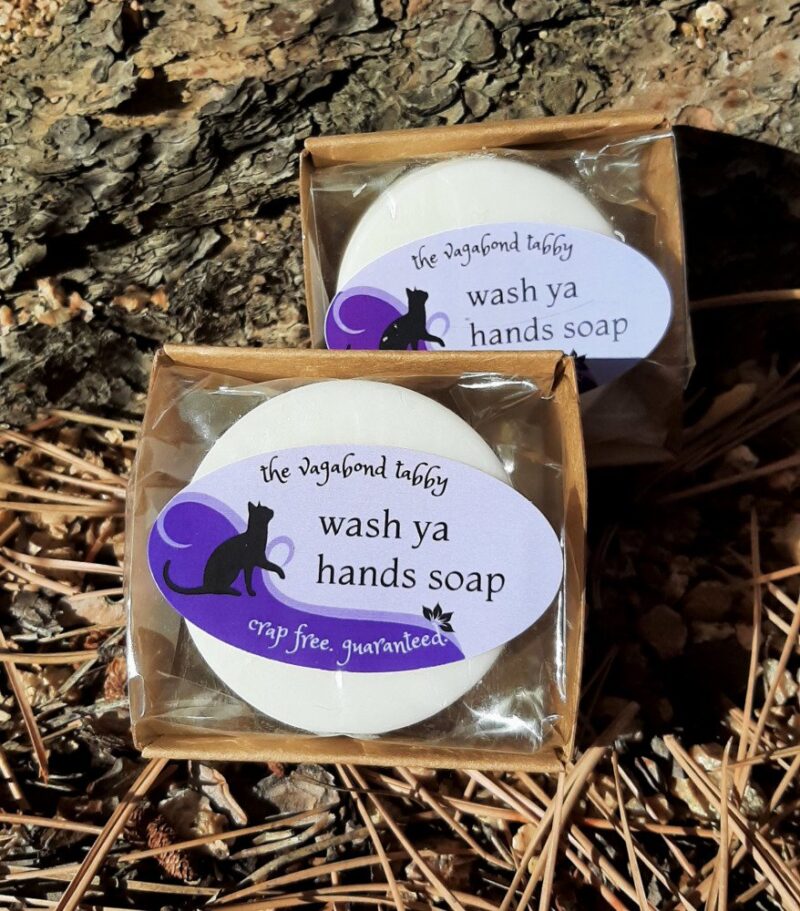 Two round bars of white soap, each encased in compostable plastic. The labels say "wash ya hands soap".