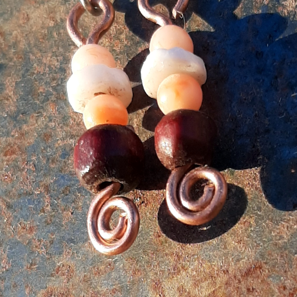 Each earring has a disc-shaped bone bead between two round peach-colored beads. below them is a round red wooden bead. All are strung on copper wire that ends at the bottom in a neat spiral.