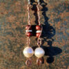 Each earring has two sections. The lower has a round white bead strung on copper wire with a neat spiral at the bottom. This is linked to a piece with a bone disc between two round red wooden beads, all strung on copper wire that curves back up around the beads, then twists around itself.