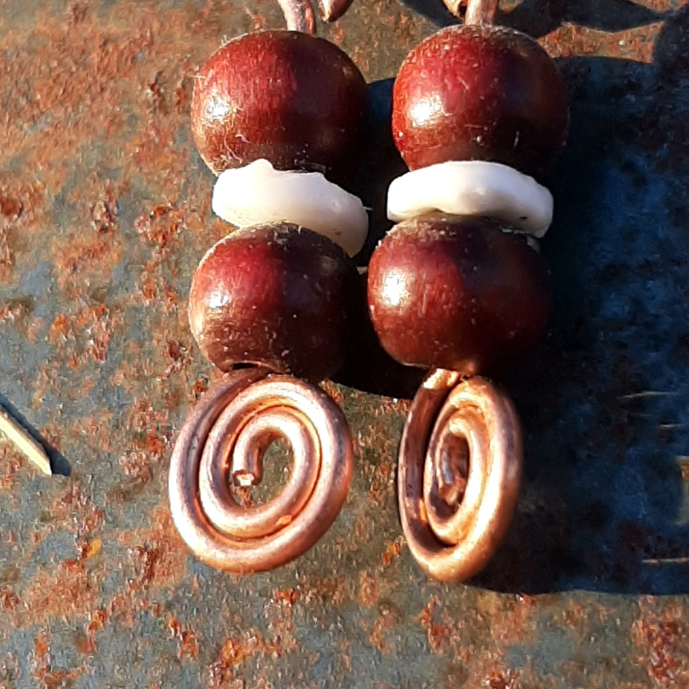 Each earring has two round red wooden beads with a disc-shaped bone bead in between. All are strung on copper wire that ends at the bottom in a neat spiral.